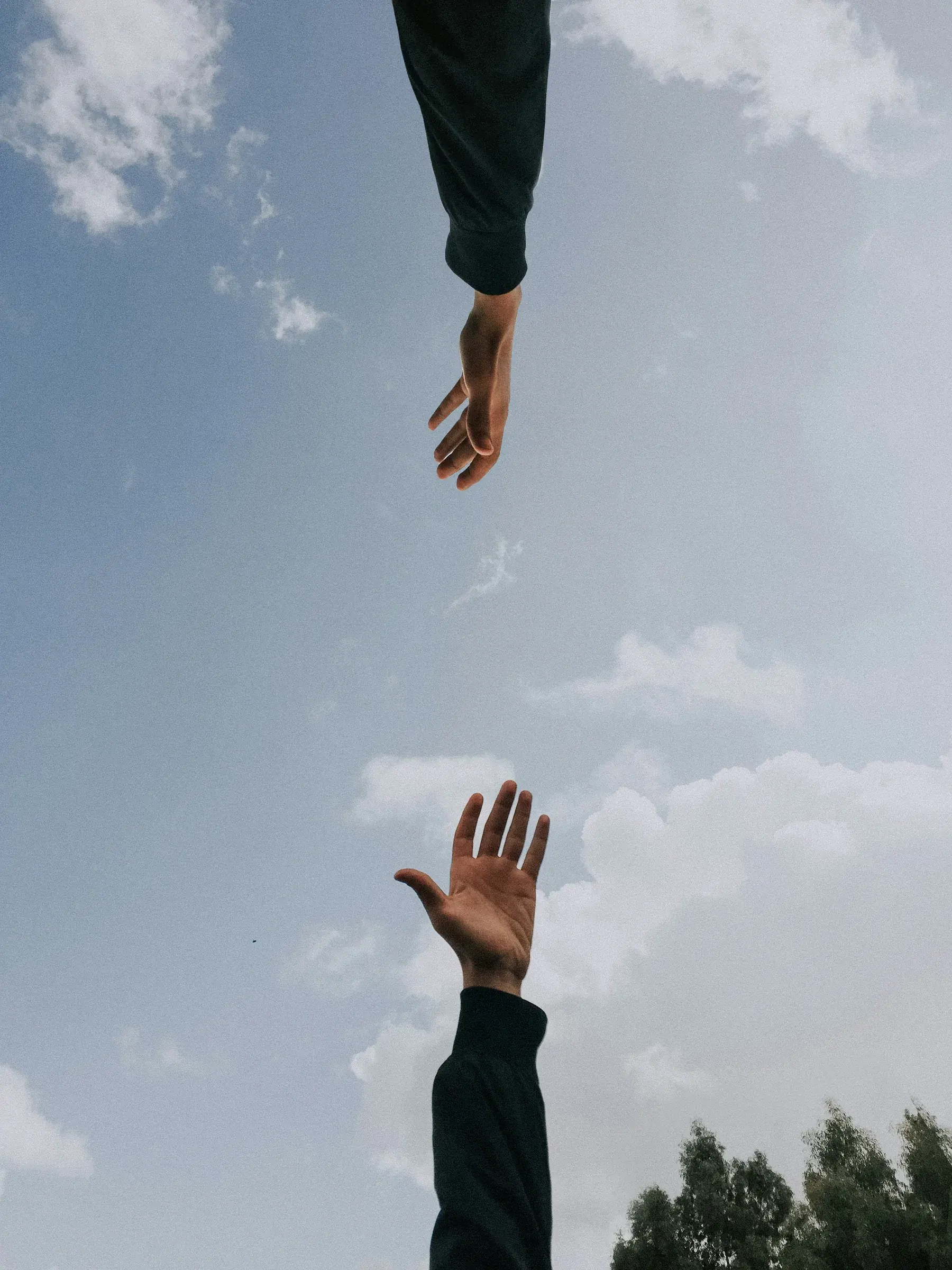 Two hands reaching towards one another against a cloudy blue sky
